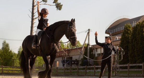 centros equestres - menina aprendendo a montar a cavalo com a ajuda de uma instrutora